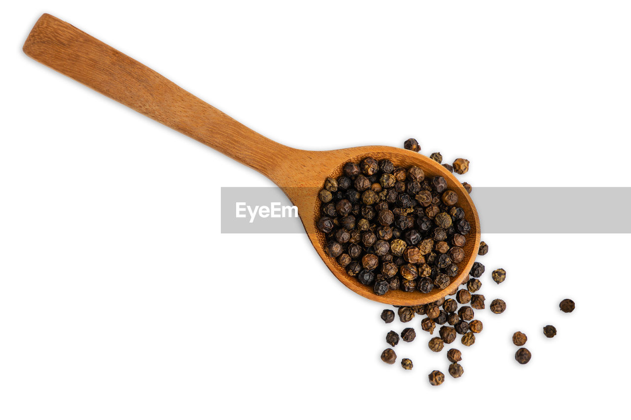 Dry black pepper in a brown wooden spoon isolated on white background. top view and clipping path.
