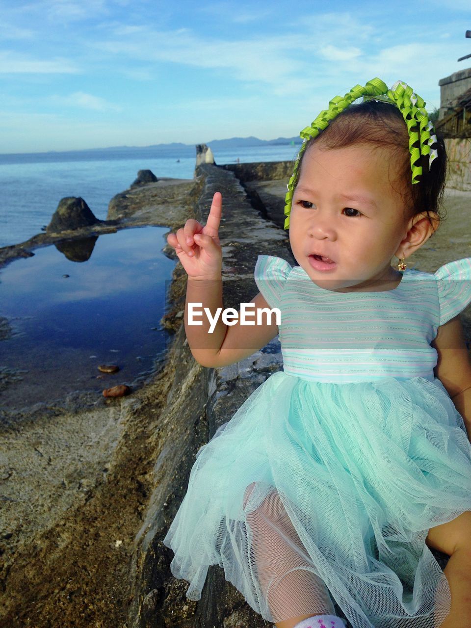 Close-up of cute girl sitting on retaining wall by sea