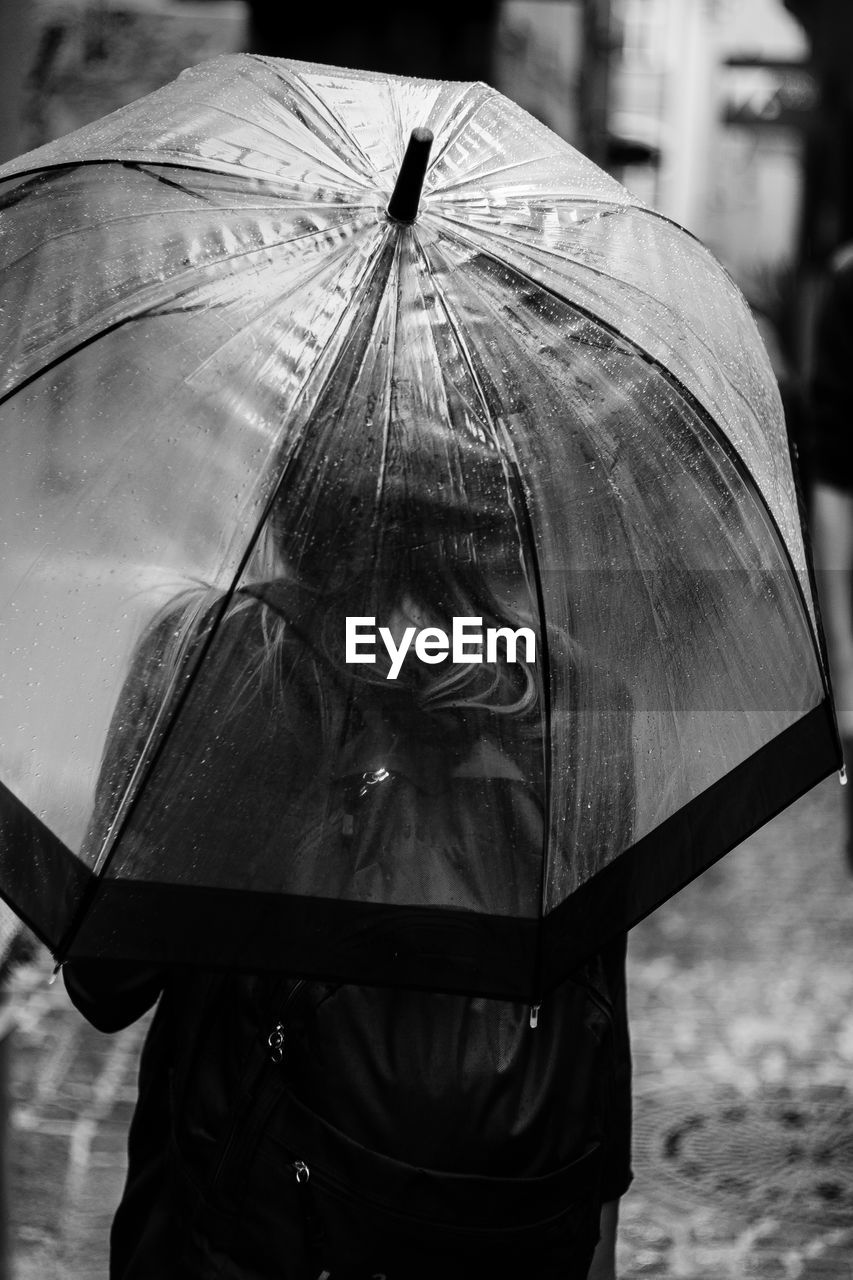 Rear view of woman under umbrella during rainy season