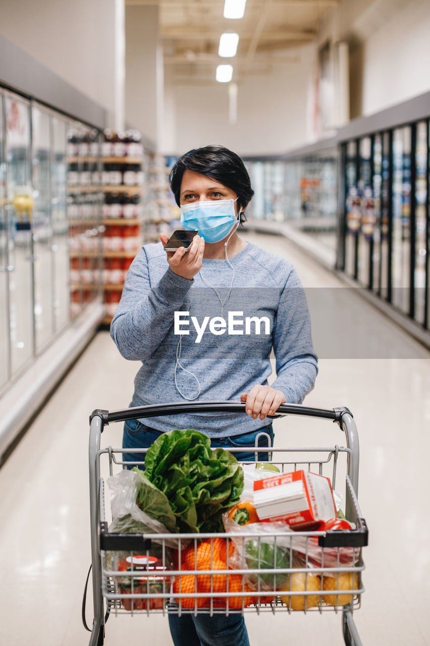 Middle age brunette woman shopping in grocery store supermarket and talking on audio chat phone. 