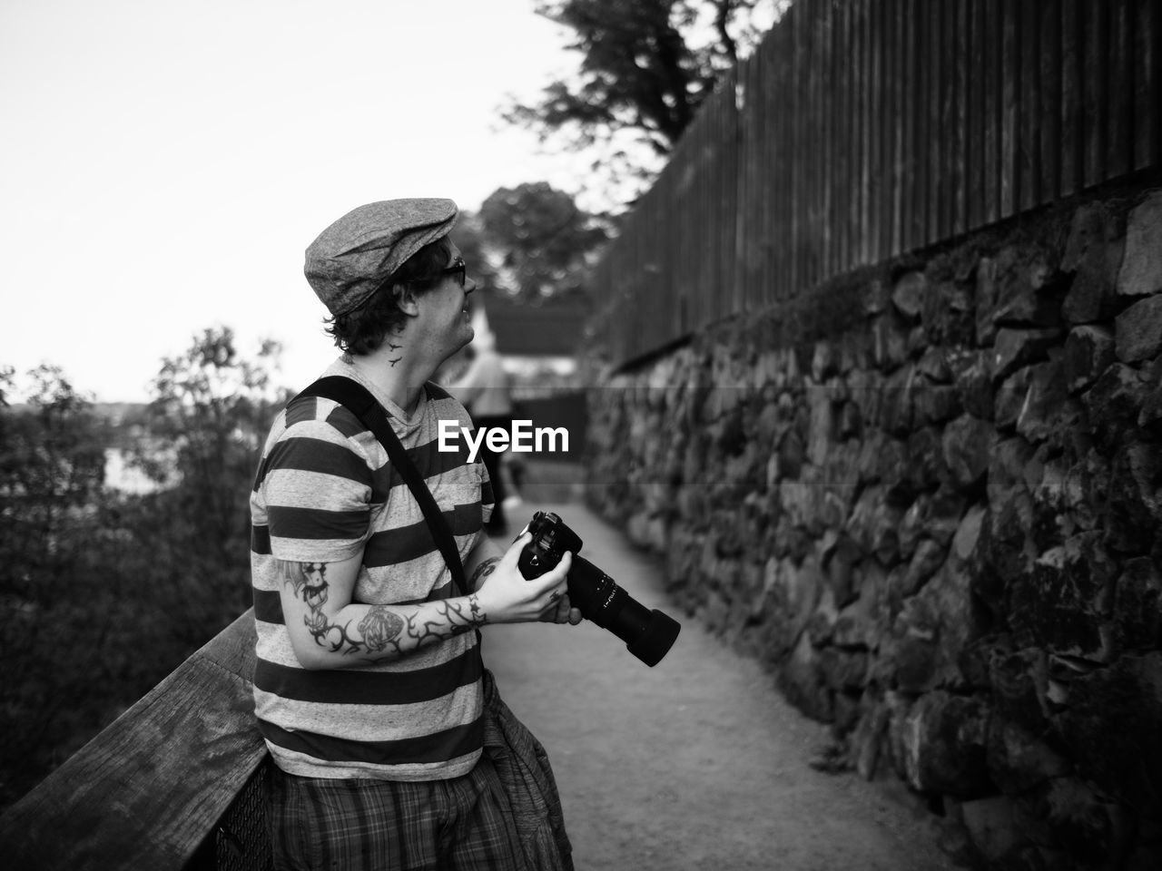 Side view of man holding camera while leaning on railing at footpath