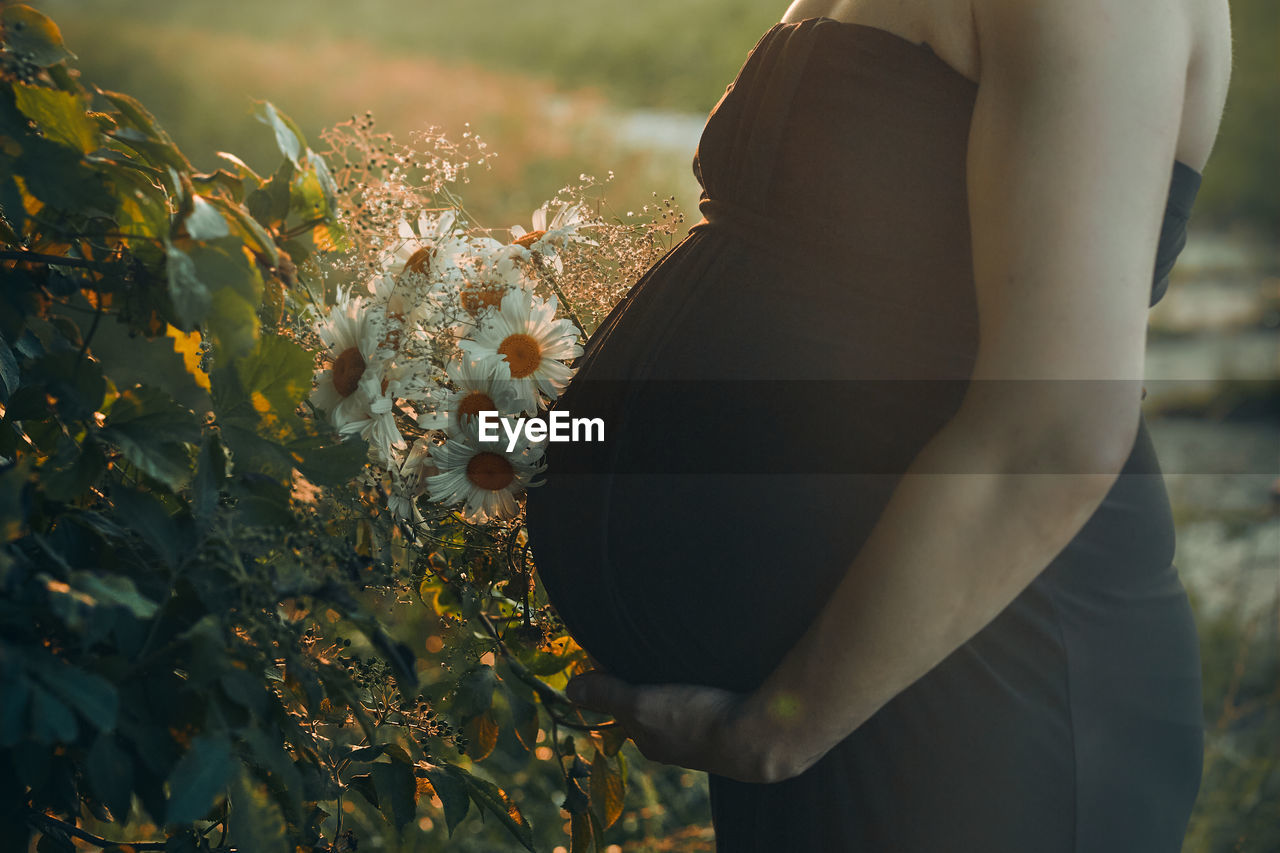 Pregnant woman hugging her tummy standing outdoors surrounded by nature. pregnancy, expectation
