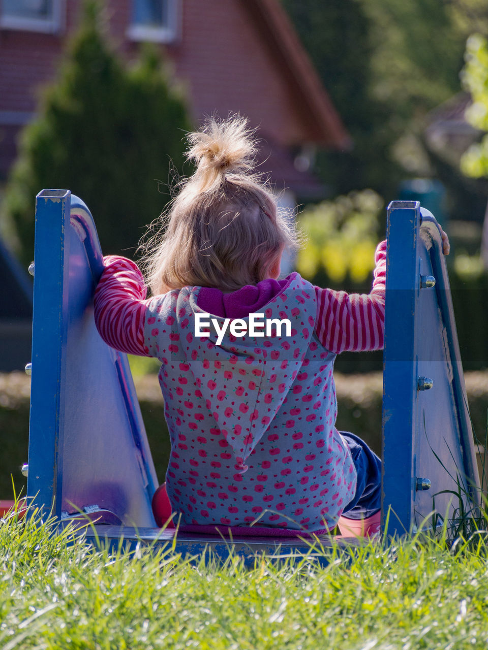 Rear view of girl sitting on slide at playground