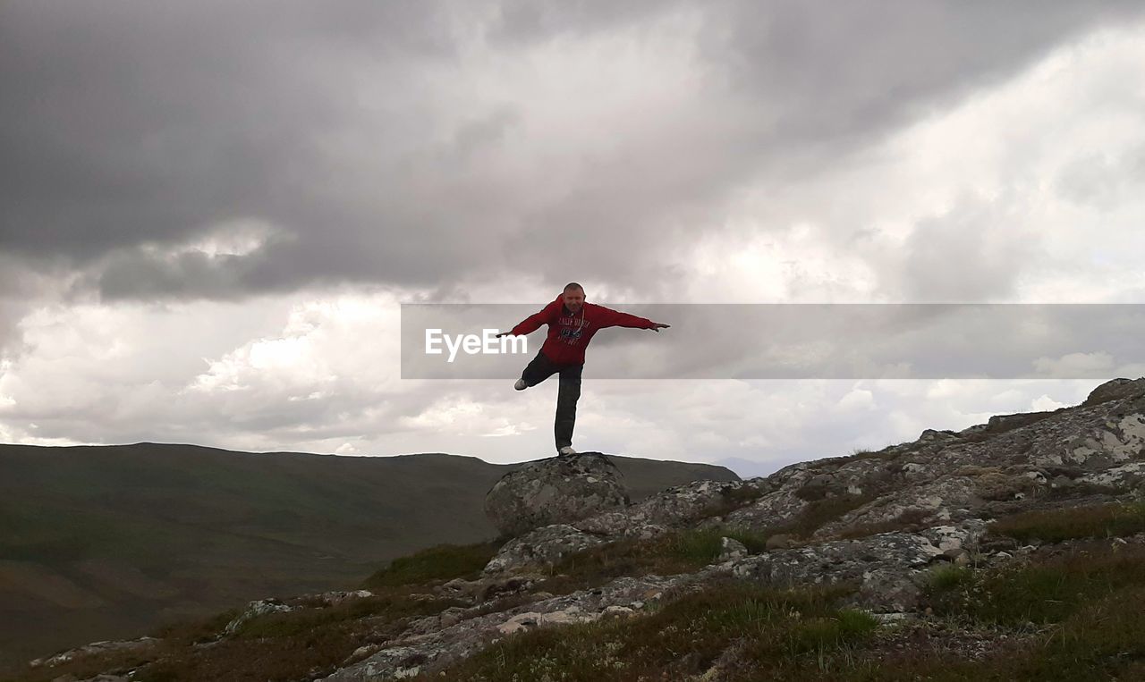 MAN STANDING ON ROCK WITH MOUNTAIN IN BACKGROUND