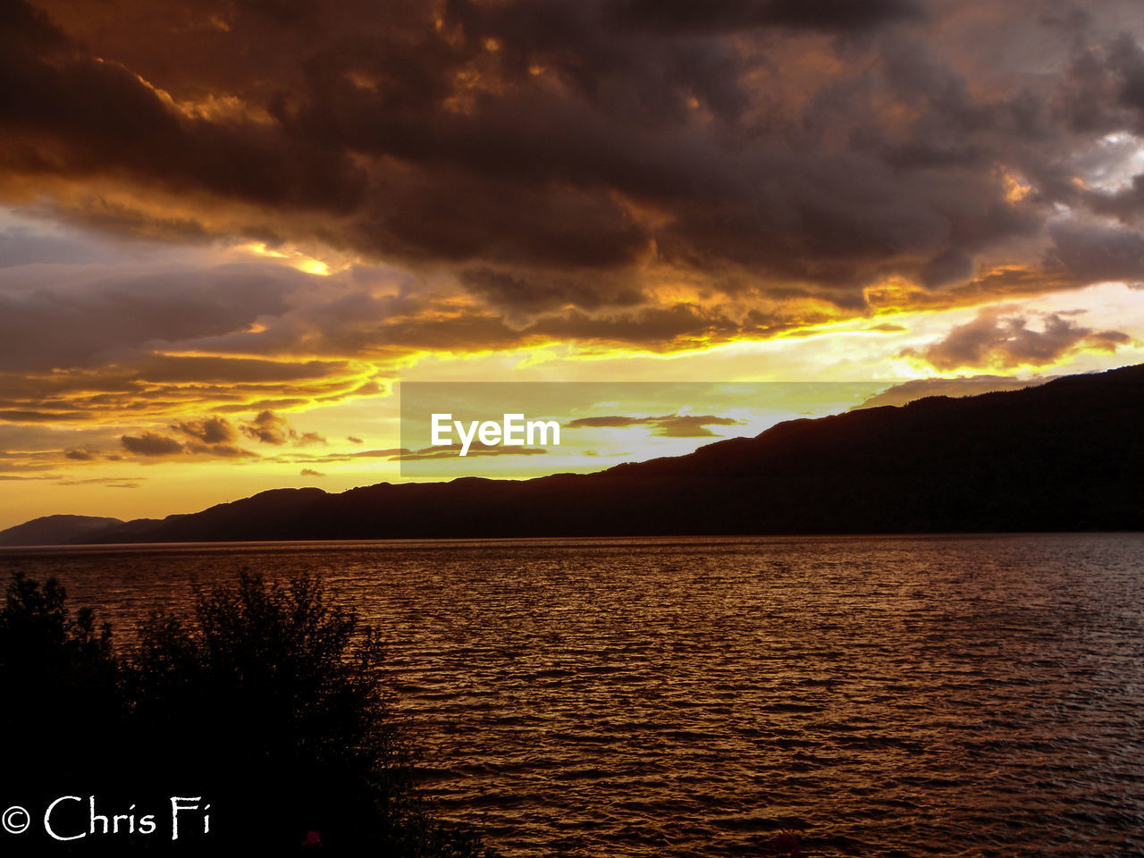 SCENIC VIEW OF LAKE BY SILHOUETTE MOUNTAINS AGAINST ORANGE SKY