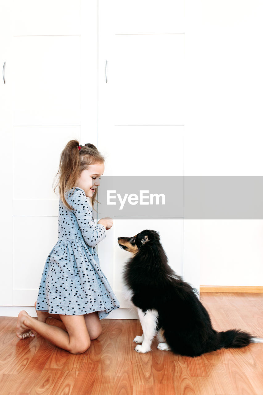 Full length of girl playing with dog at home