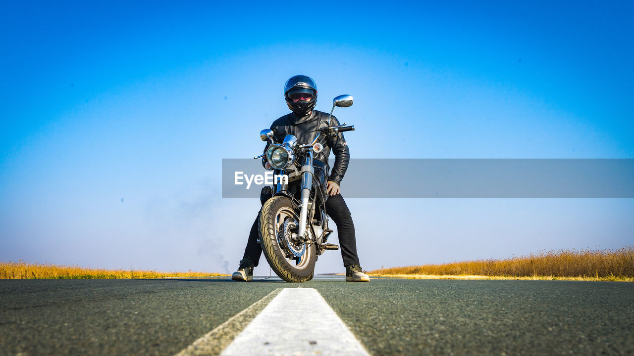 Man riding bicycle on road against clear blue sky