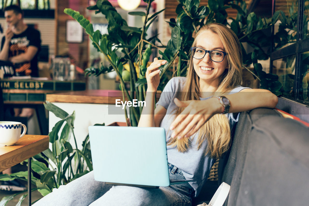 Young energetic successful positive woman with laptop on sofa in cafe.