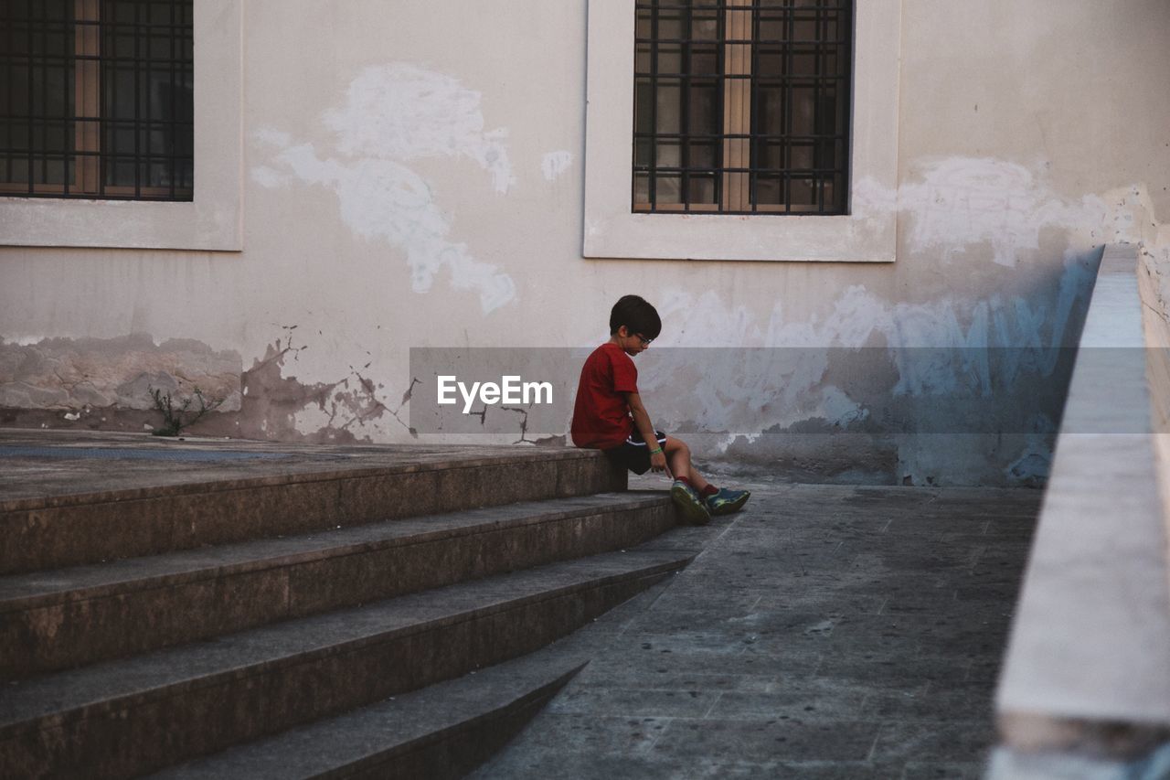 Boy sitting on steps against building