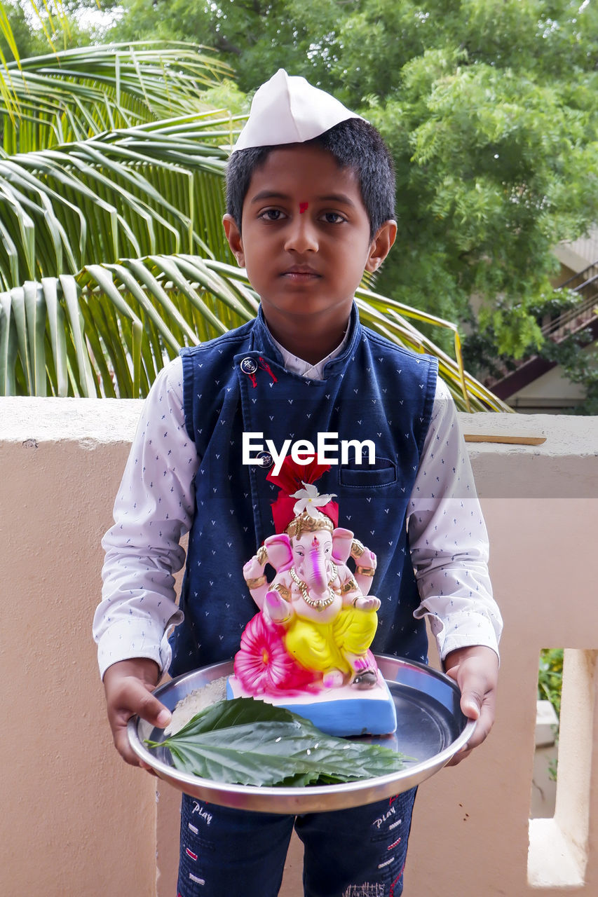 Portrait of boy holding ganesh statue standing at balcony