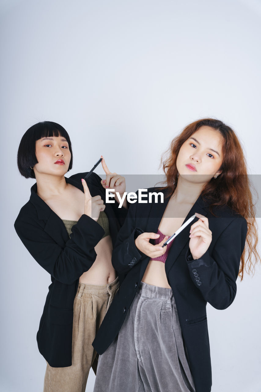 Portrait of lesbian couple holding pen standing against gray background