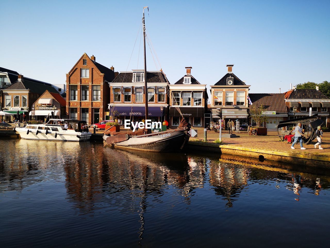 SAILBOATS MOORED IN CANAL BY BUILDINGS AGAINST SKY