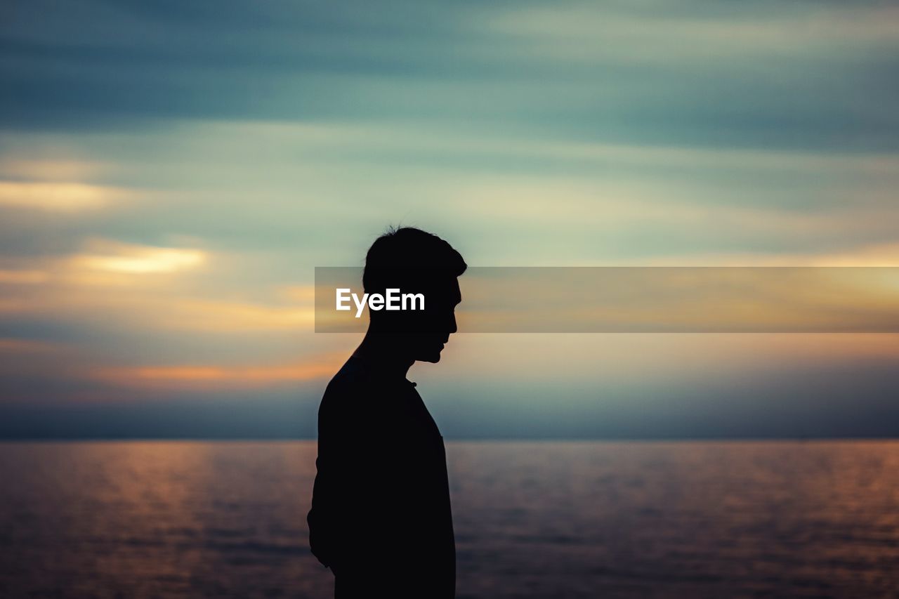 Silhouette man standing by sea against sky during sunset