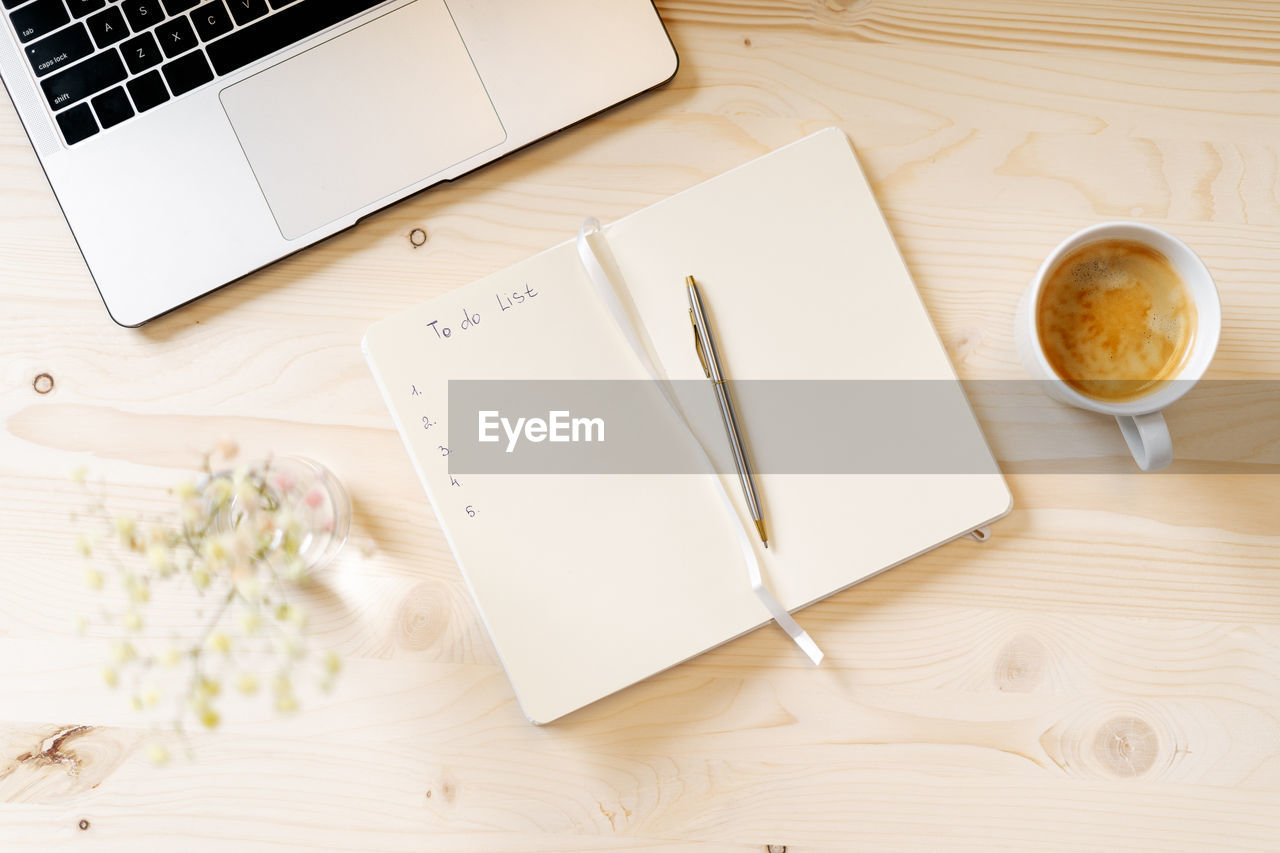 Top view blank paper notebook with to do list, laptop keyboard, cup of coffee and pen. desktop mocku