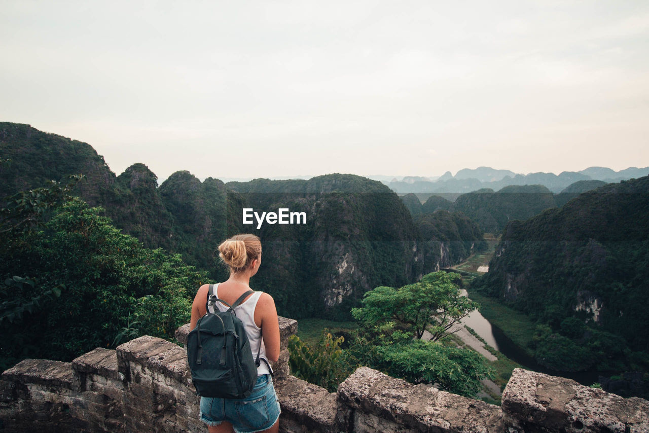 Rear view of woman with backpack looking at mountains against sky