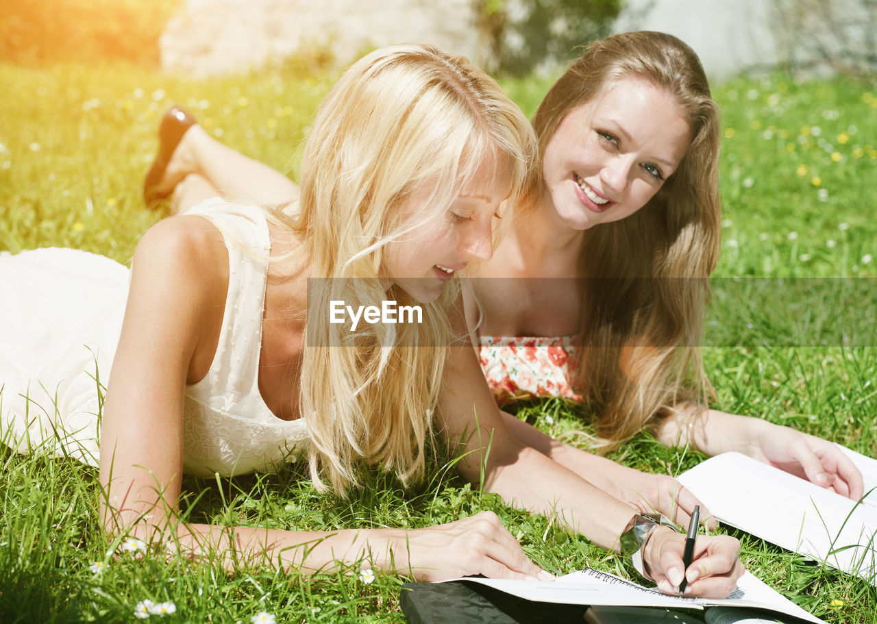 Portrait of smiling woman with friend writing in book at park