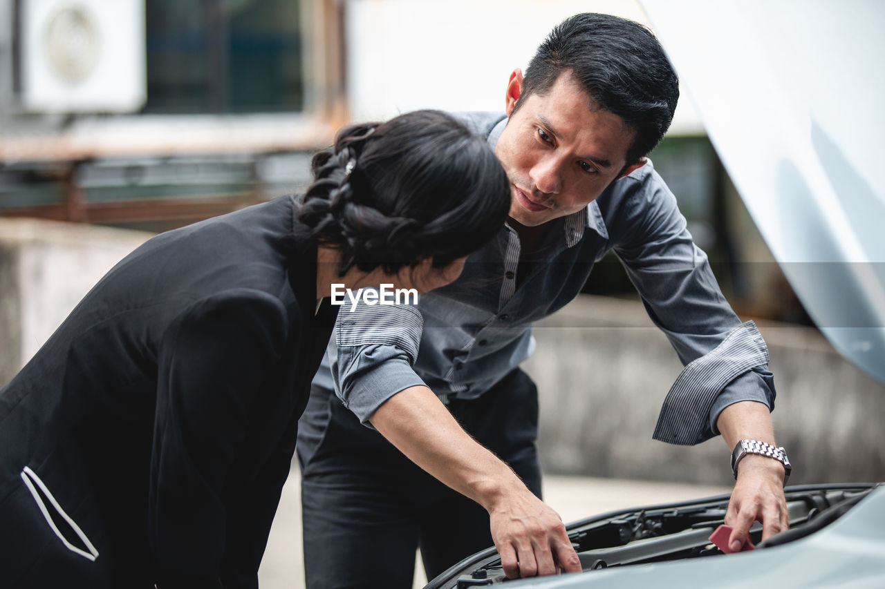 Man assisting woman to repair car