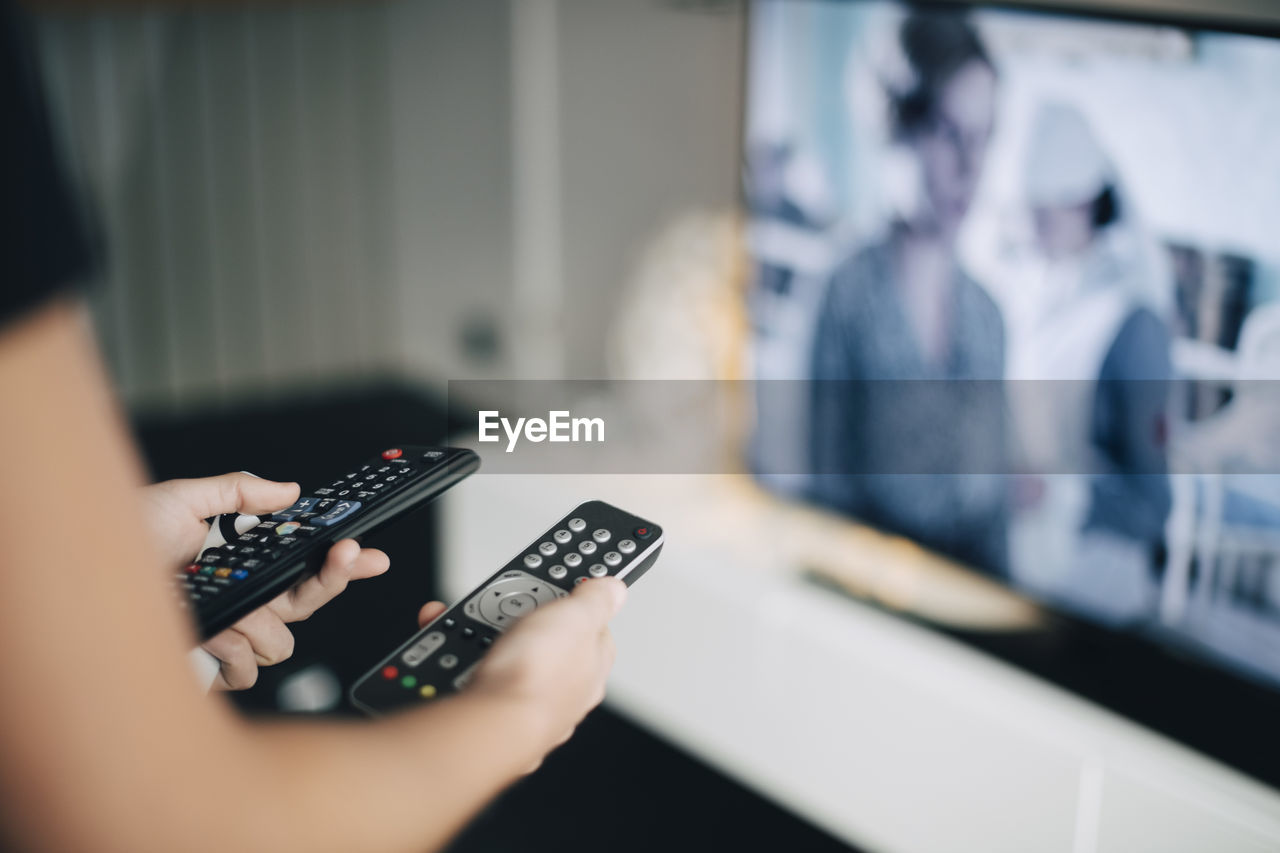 Midsection of teenage girl holding remote controls by television set in living room at home