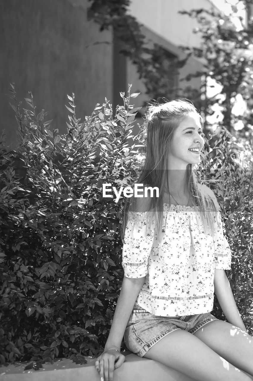 Young woman smiling while sitting on bench by plants