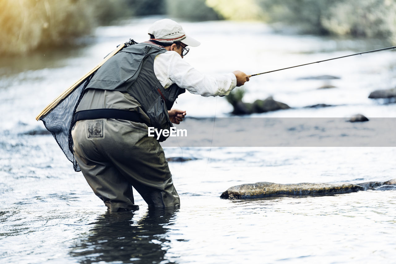 SIDE VIEW OF A MAN FISHING ON RIVER