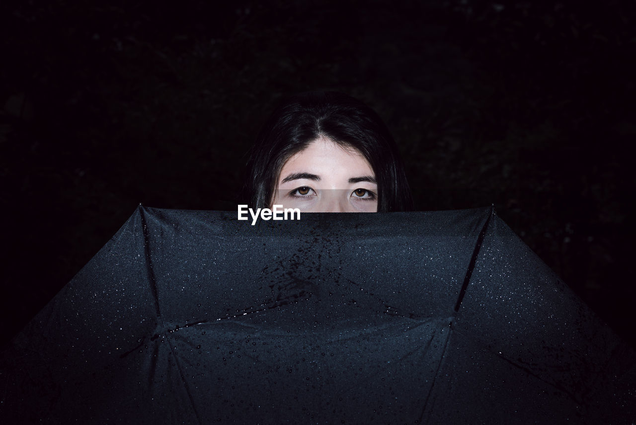 Portrait of young woman with wet umbrella standing outdoors at night