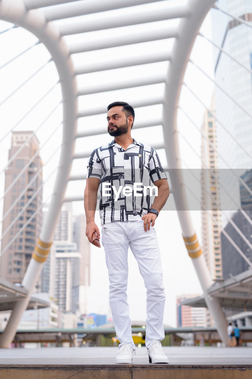 FULL LENGTH PORTRAIT OF YOUNG MAN STANDING ON CITY