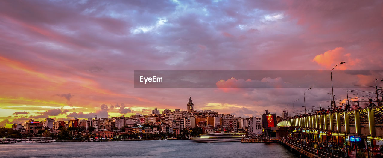 Galata bridge over river leading towards cityscape against cloudy sky during sunset