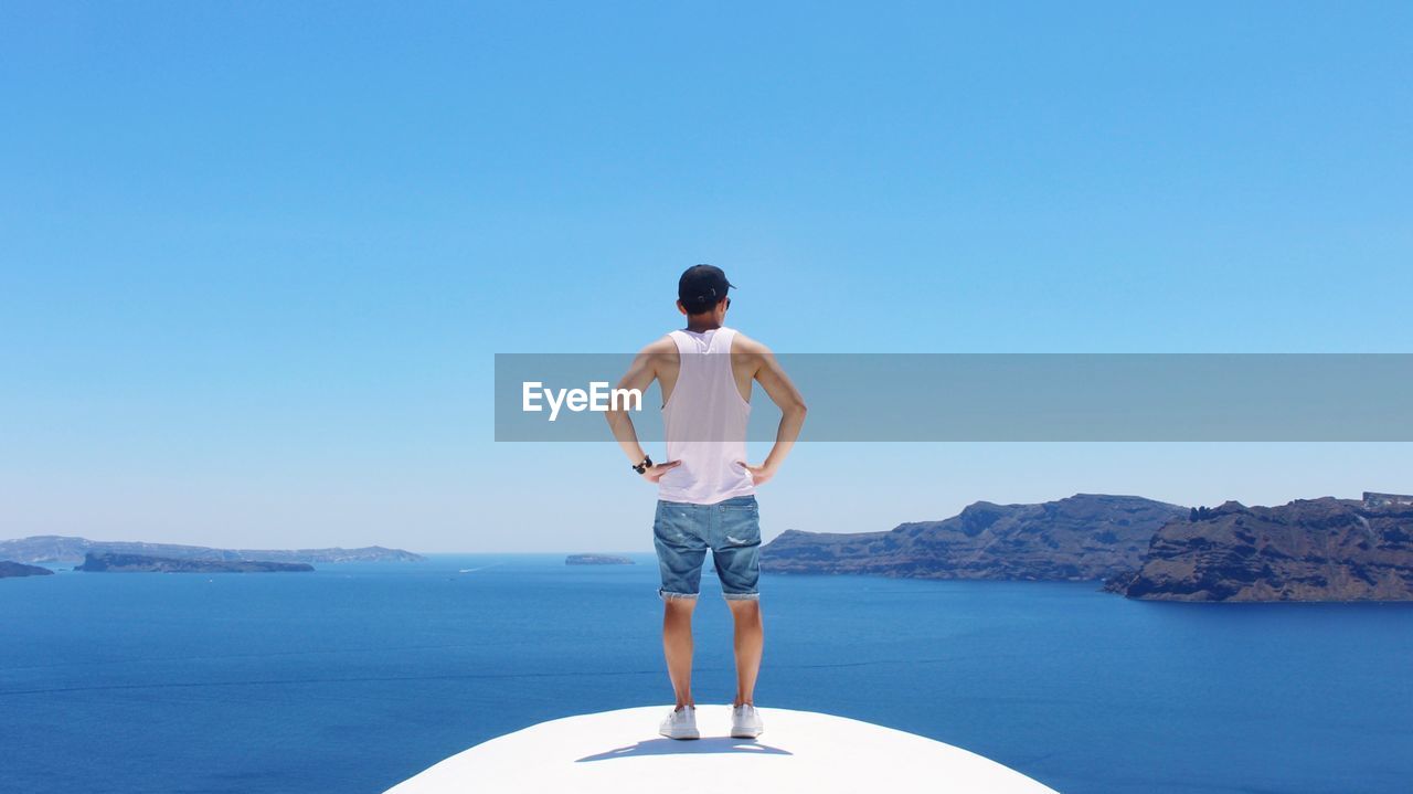 Rear view of man standing on boat in sea against clear blue sky