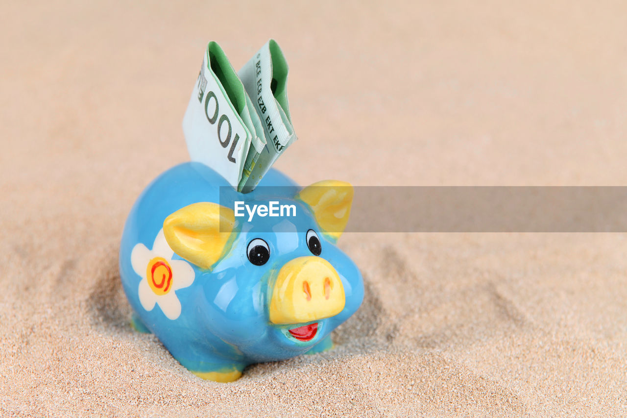 Close-up of paper currency in piggy bank on sand