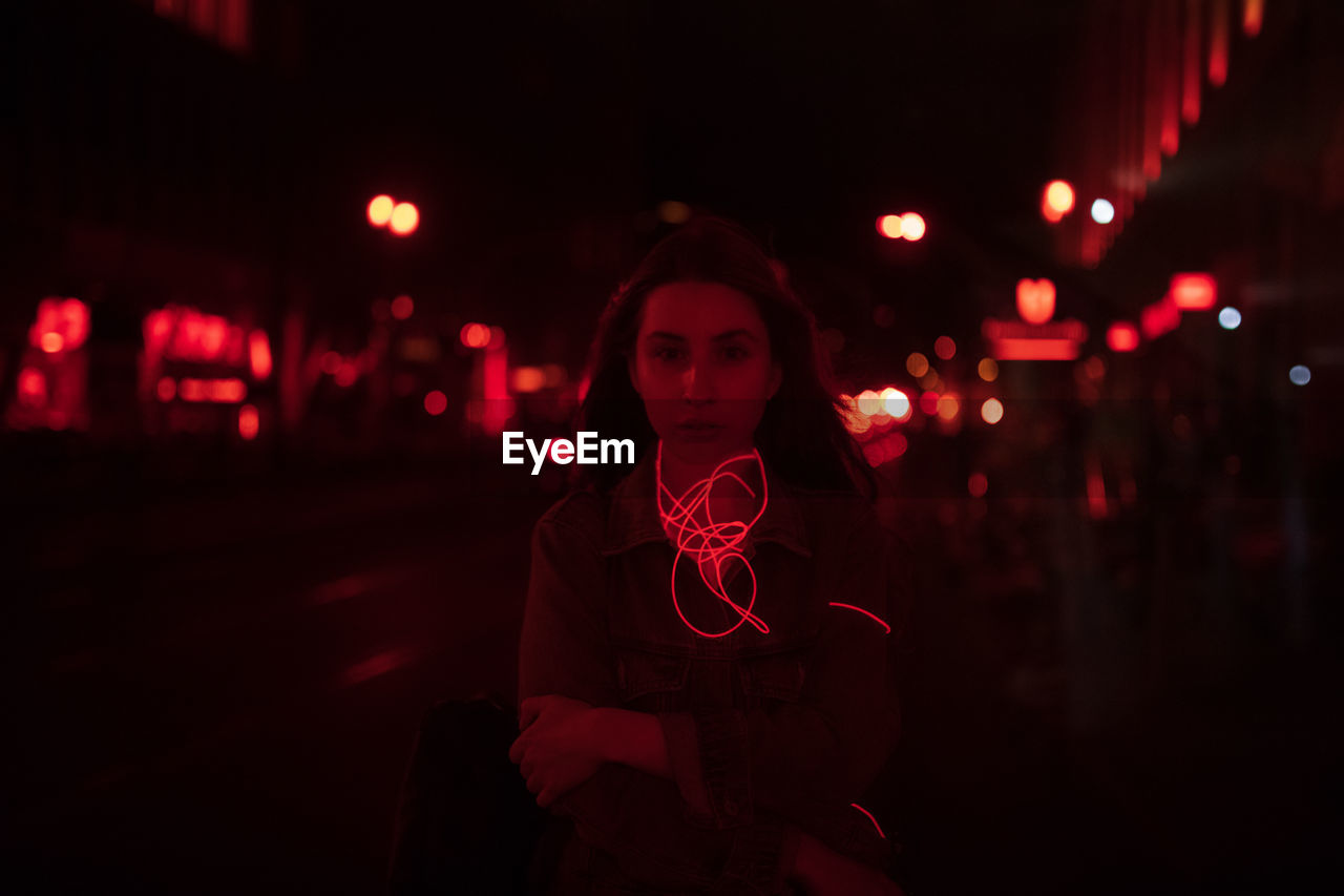 Portrait of young woman standing on road at night