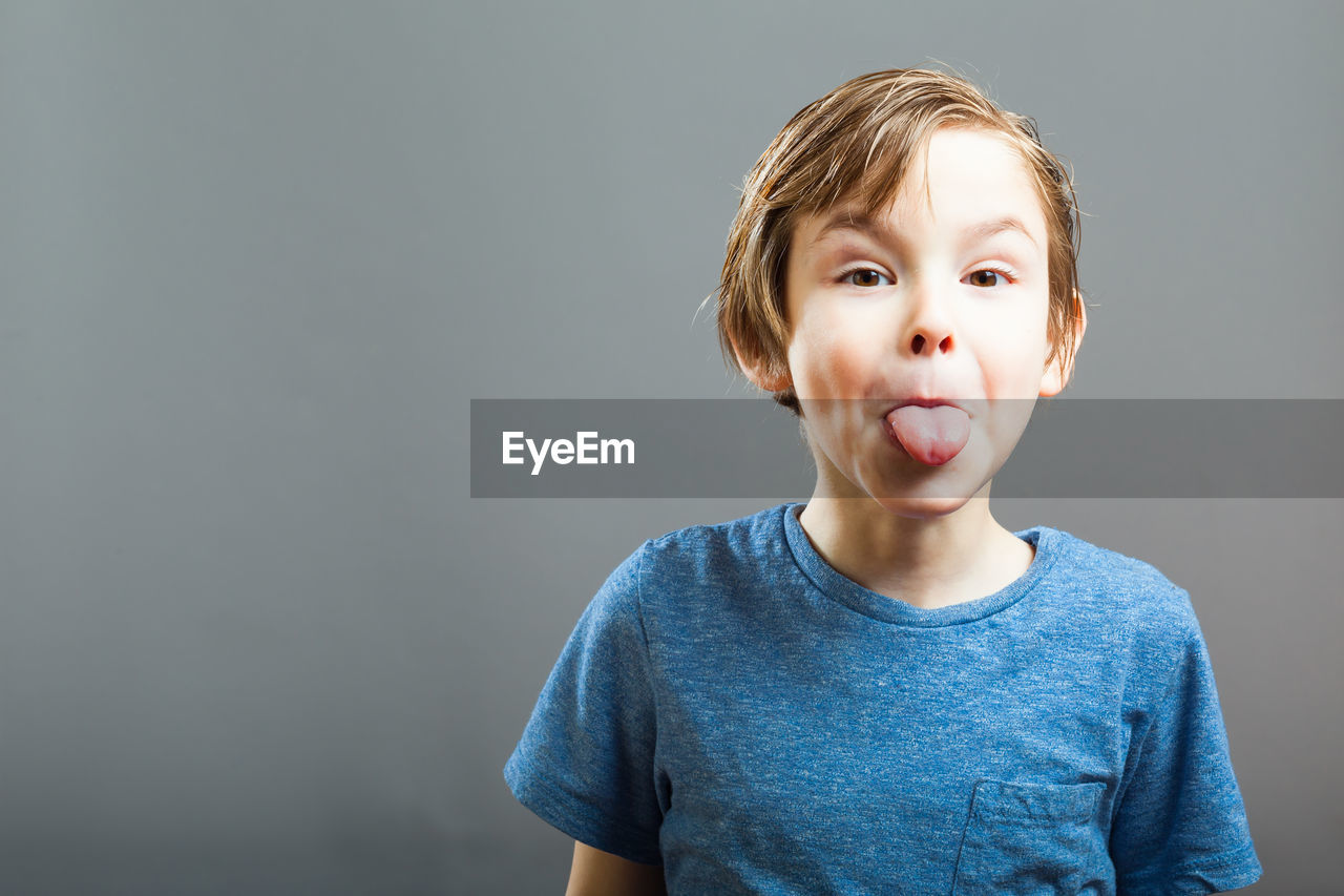 Portrait of playful boy sticking out tongue against gray background