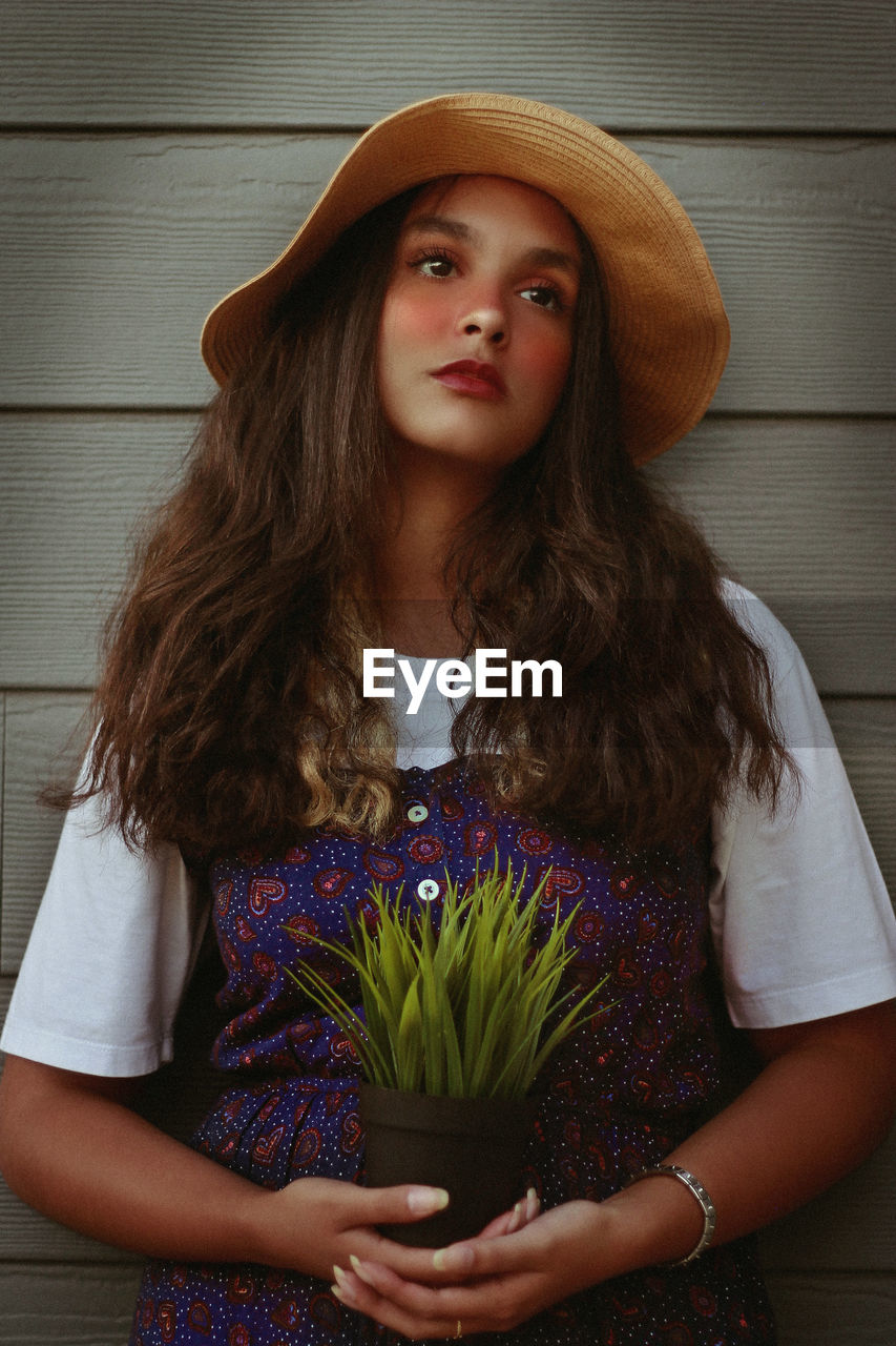 Teenage girl wearing hat looking away while standing against wood paneling