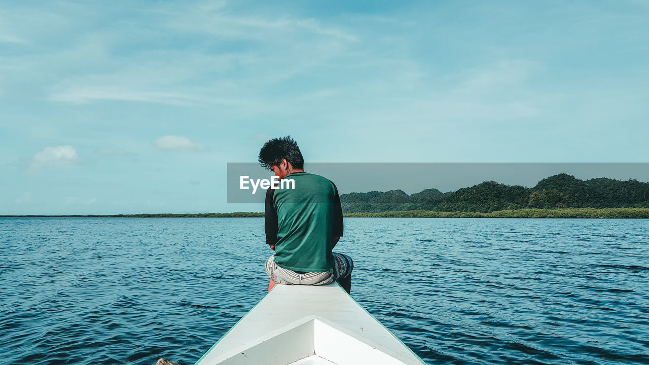 Rear view of man sitting on boat in sea against sky