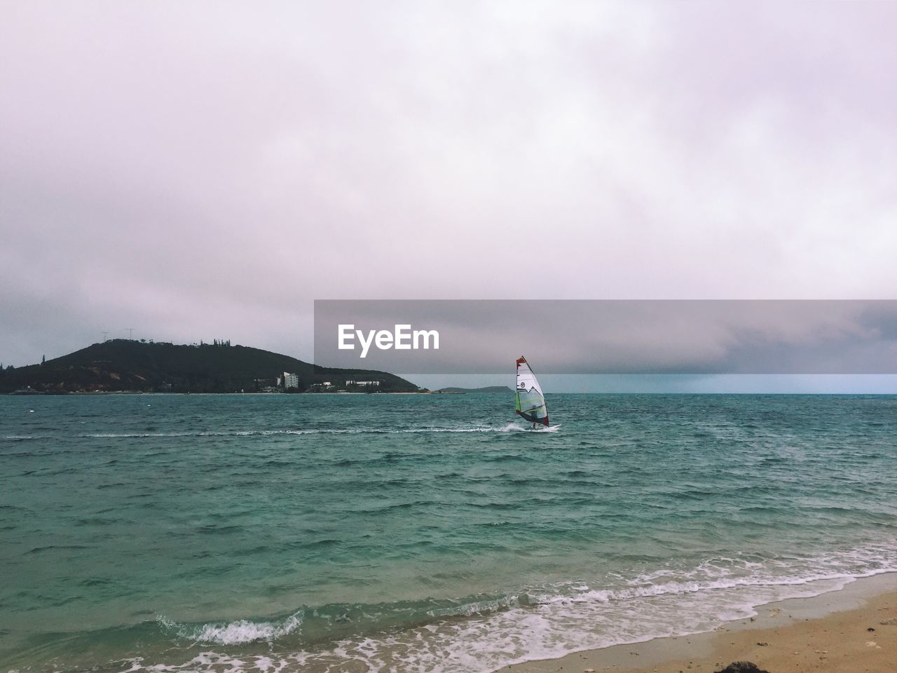 Person windsurfing in sea against cloudy sky