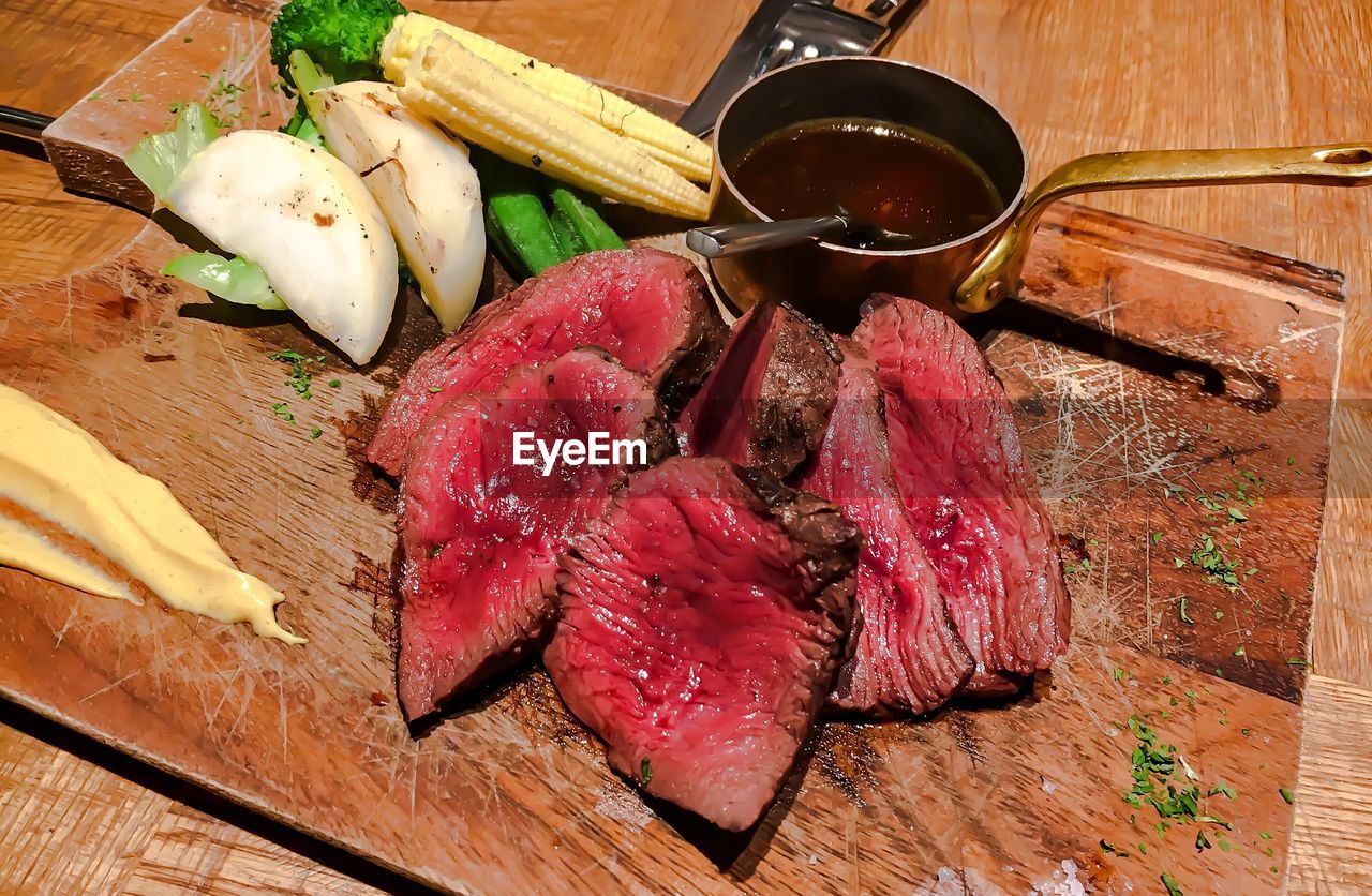 High angle view of raw beef steak on cutting board along with vegetables