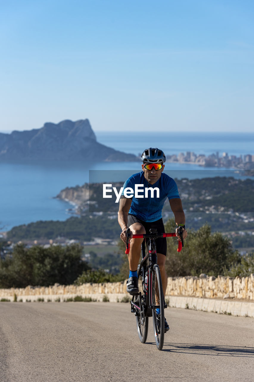 Cyclist climbing cumbre del sol hill with view of mediterranean sea.