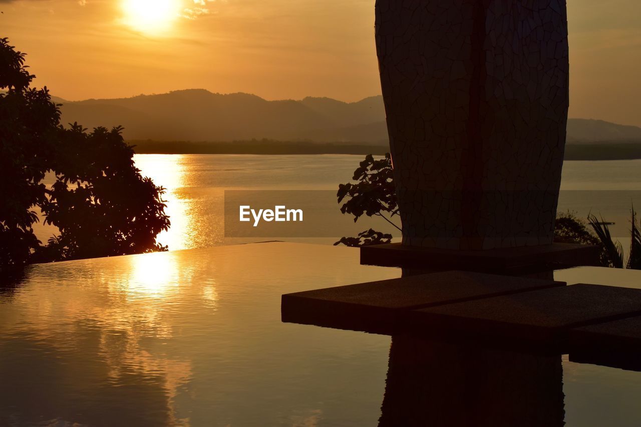 SILHOUETTE TREE BY LAKE AGAINST ORANGE SKY