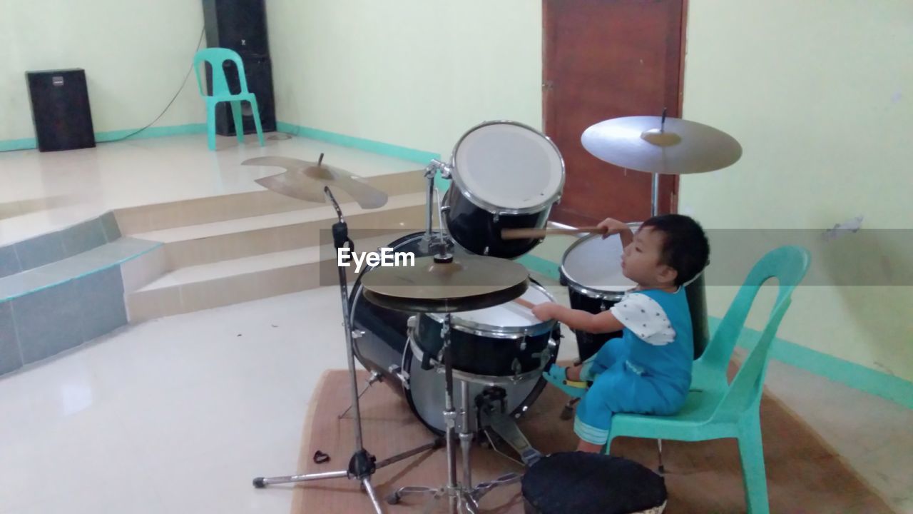 REAR VIEW OF BOY SITTING ON TABLE AT HOME