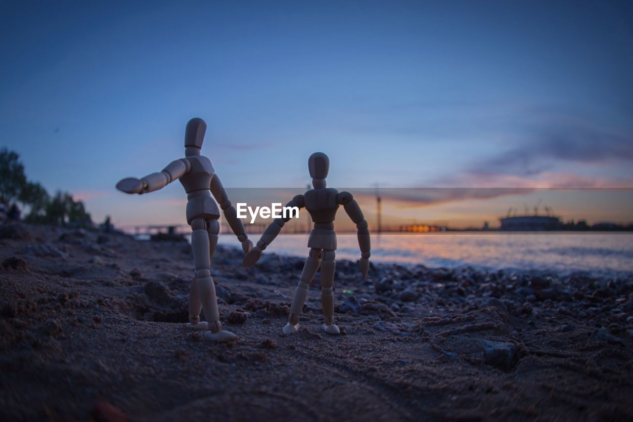 Close-up of wooden figurines on beach against sky during sunset