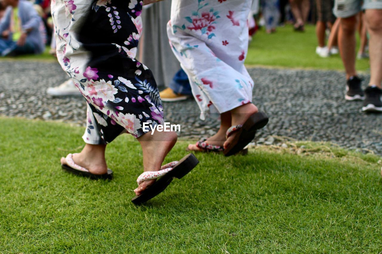 Low section of japanese women walking on grassy field