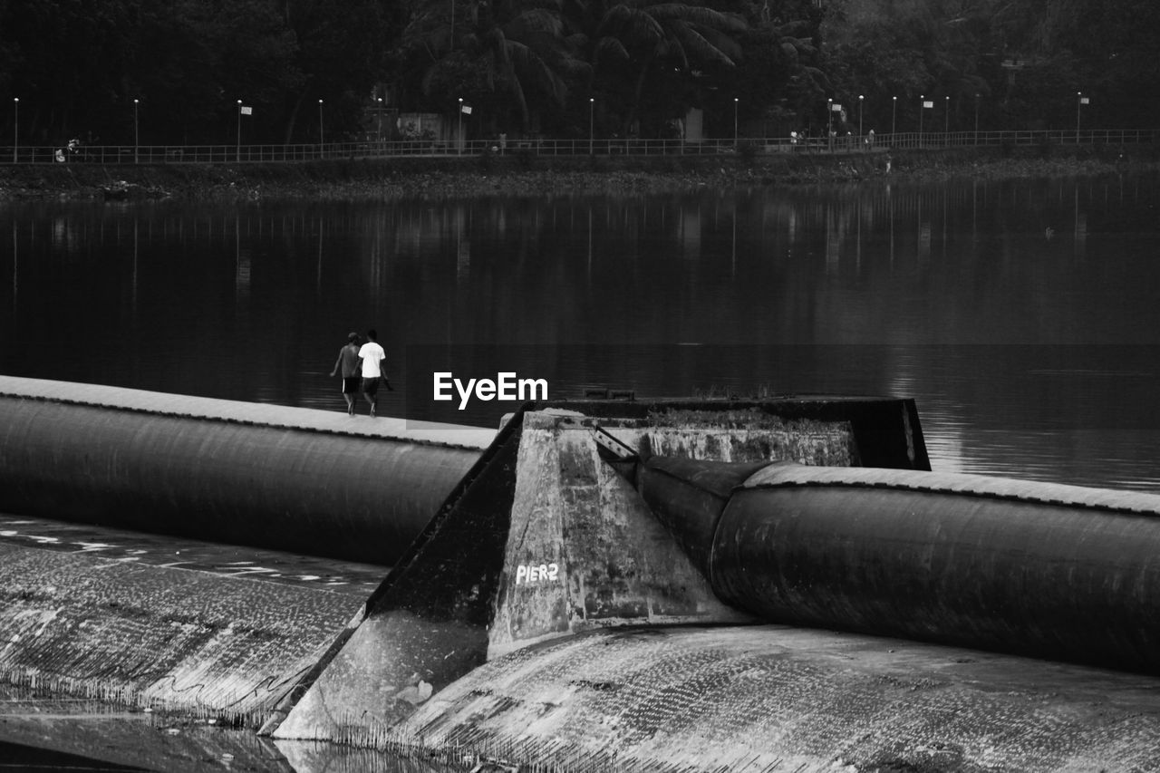 Friends walking on pipe by river