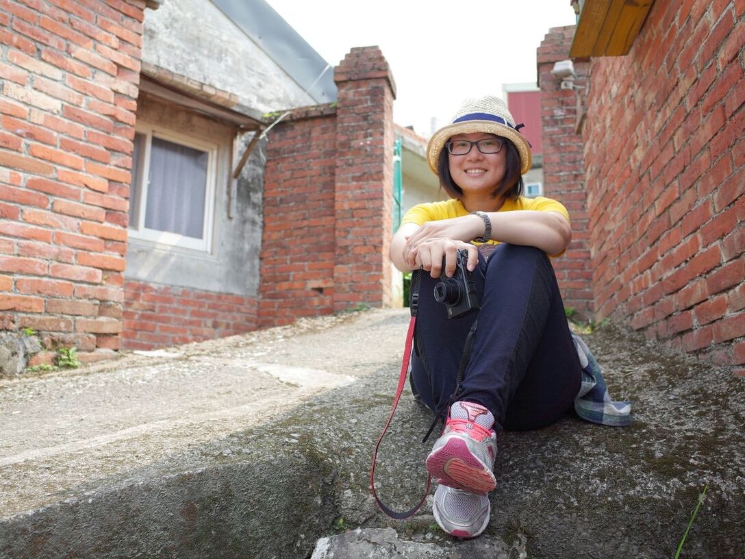 Portrait of woman holding camera while sitting on footpath