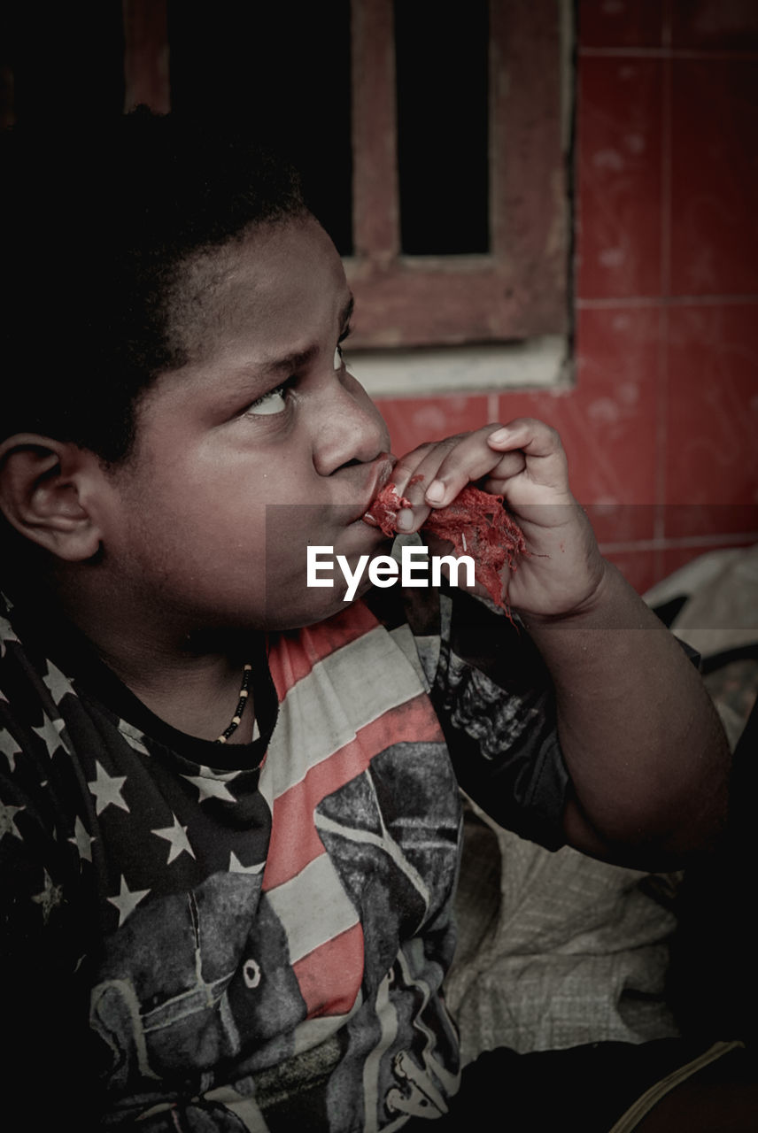 CLOSE-UP PORTRAIT OF BOY EATING FOOD IN KITCHEN