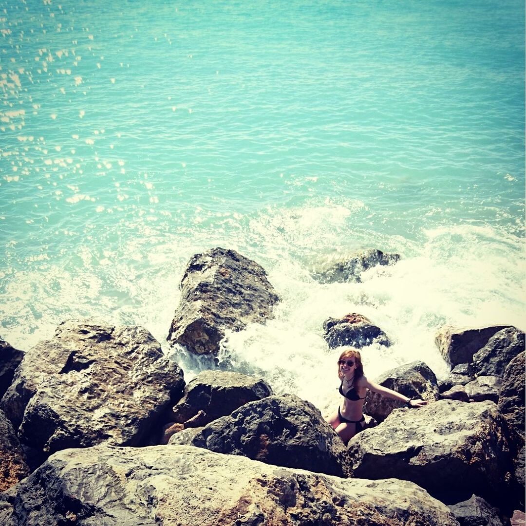 High angle view of young woman in bikini sitting on rock by sea