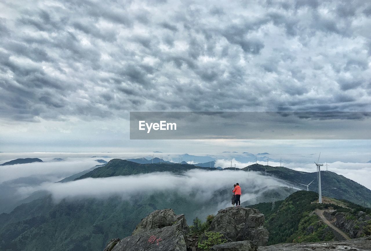 Rear view of couple standing on cliff by mountains