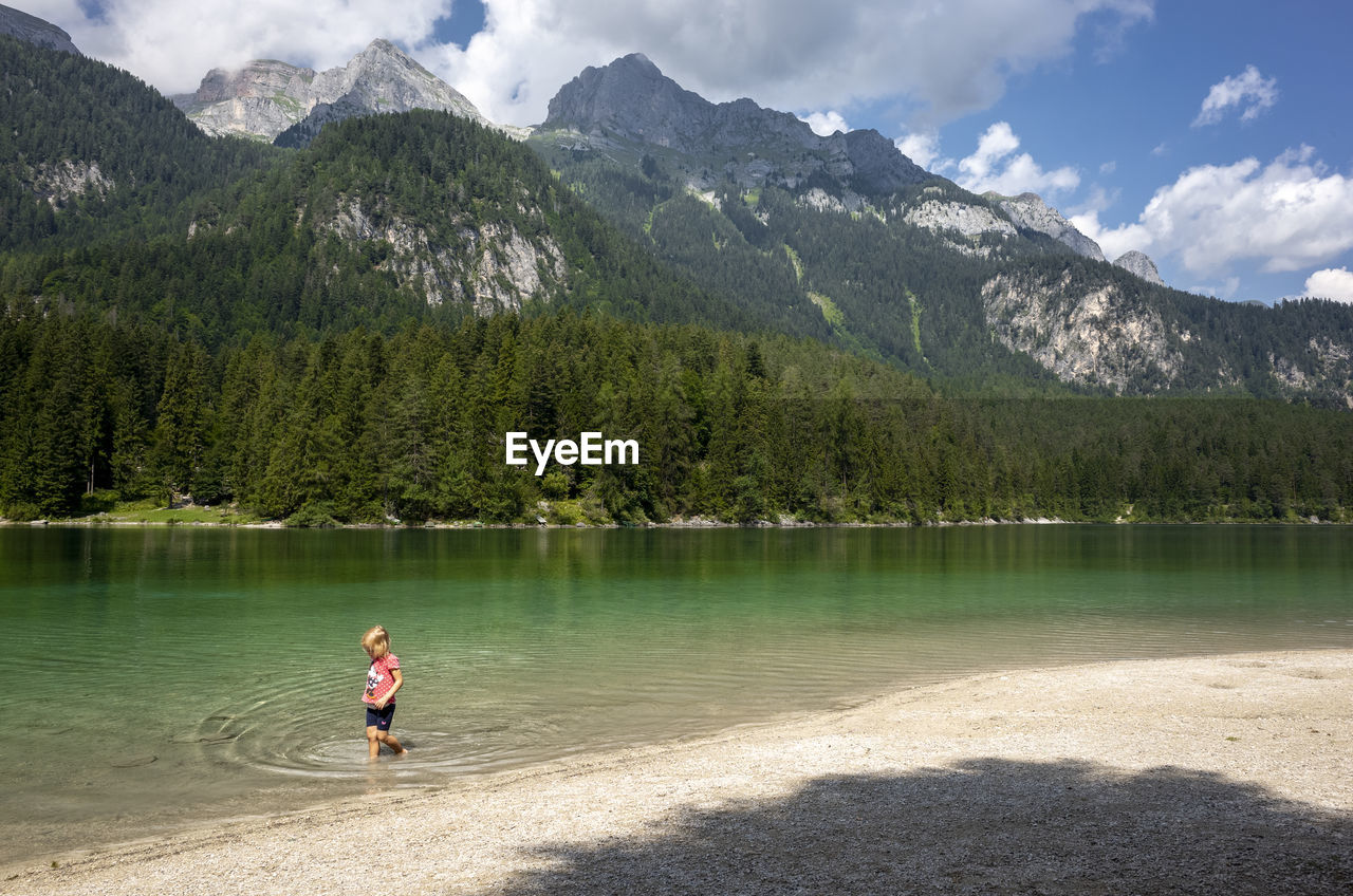 Side view of girl wading in lake by mountains