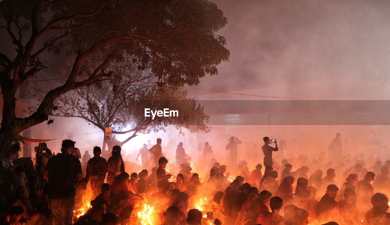 People are praying at rakher upobash under big tree in a smokey environment