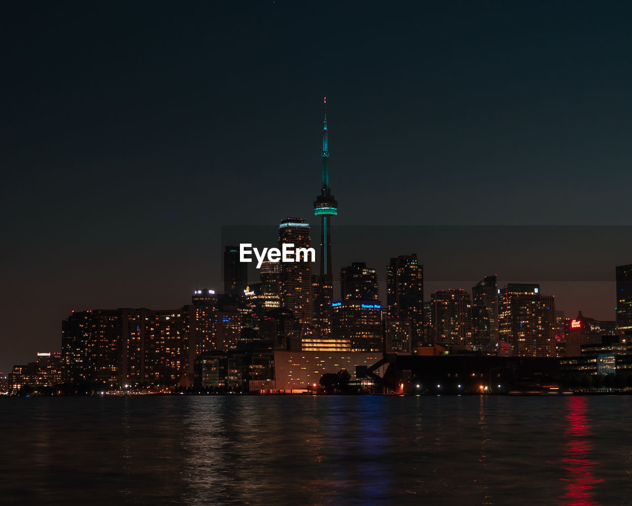 Illuminated buildings by river against sky at night