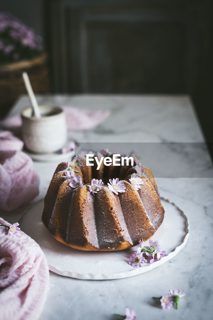 From above of tasty bundt cake decorated with fresh flowers and served on plate on table in kitchen