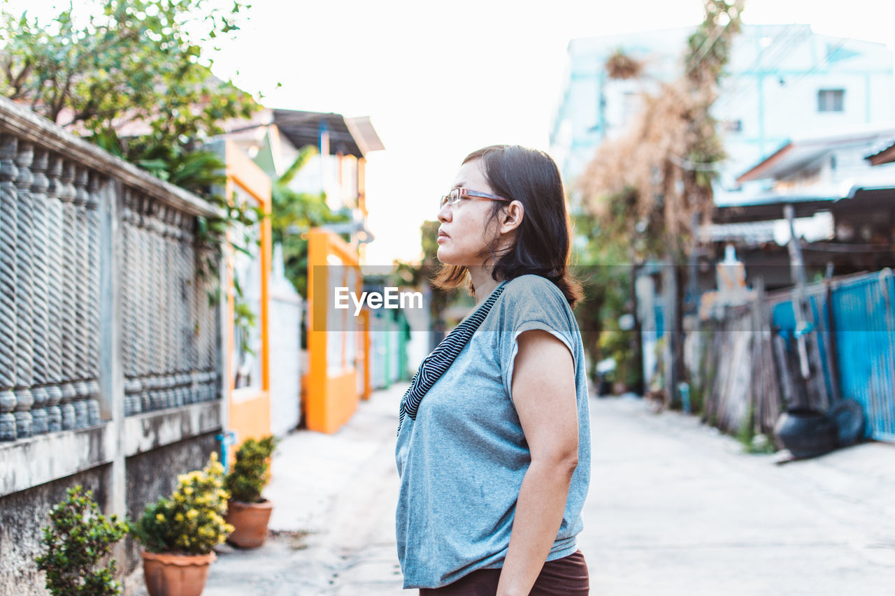 Side view of young woman looking away against buildings